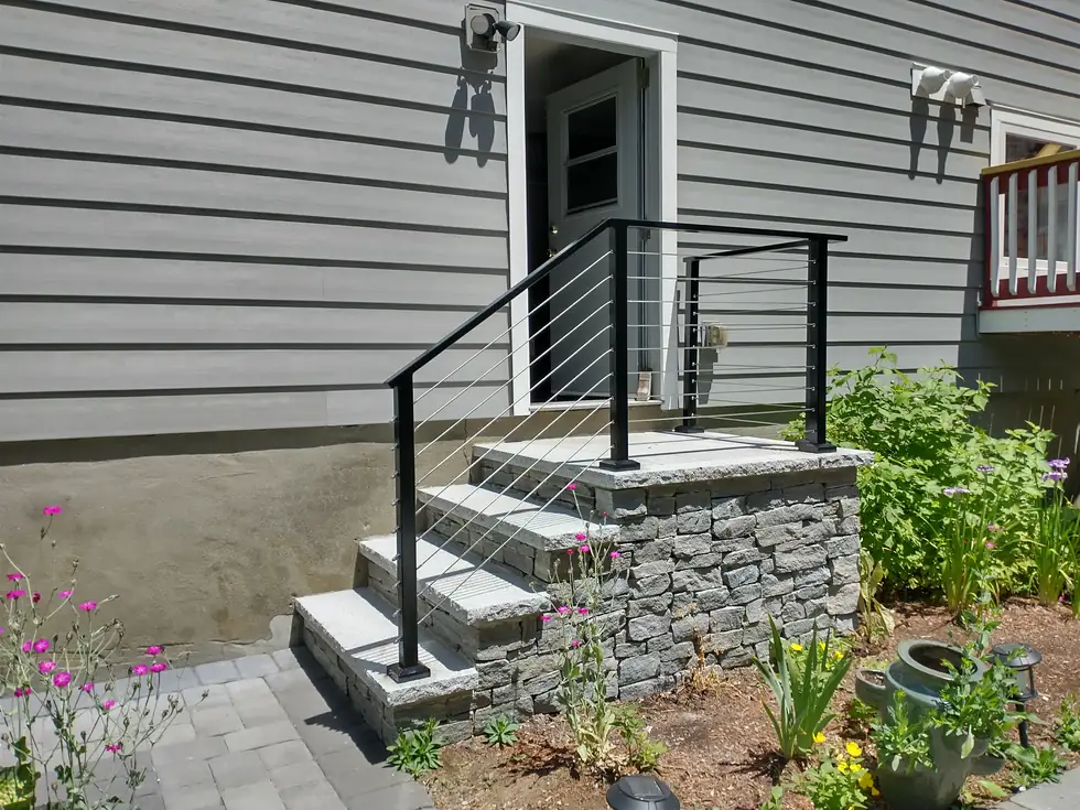 Black cable handrail on entry steps beside a garden