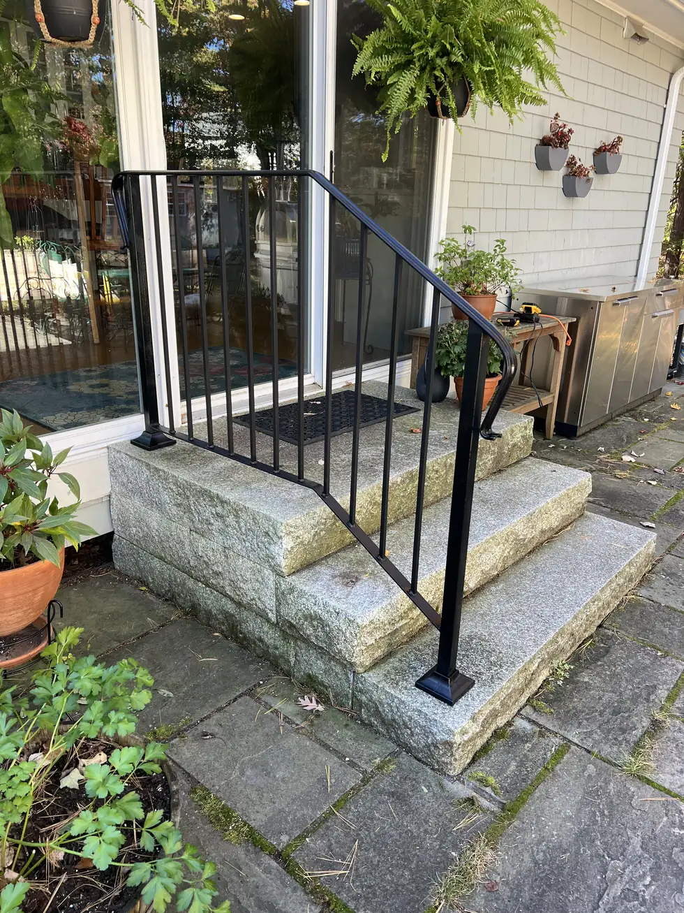 Black handrail on granite steps at a rear entry