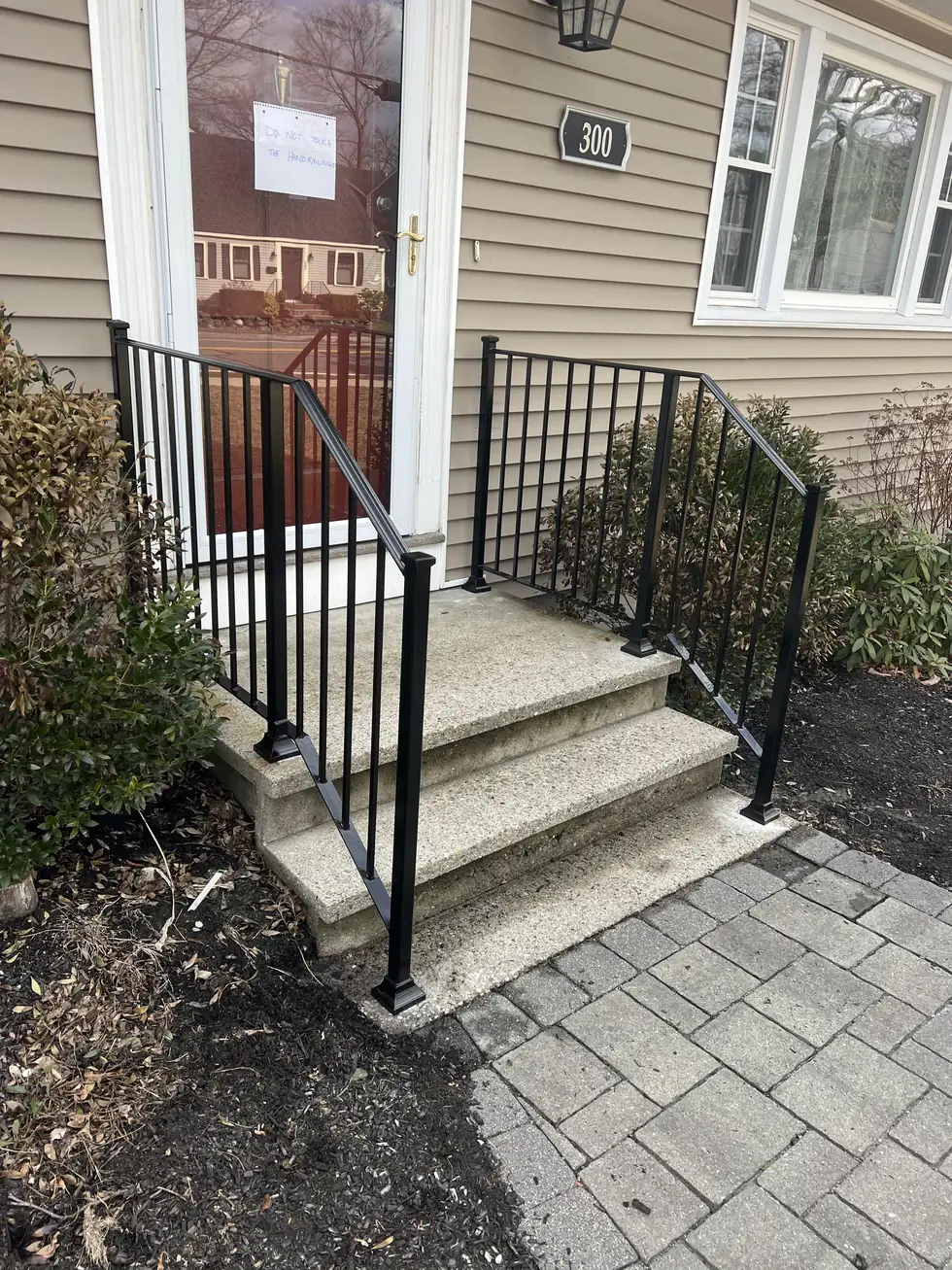 Black iron handrail on concrete steps at a tan house