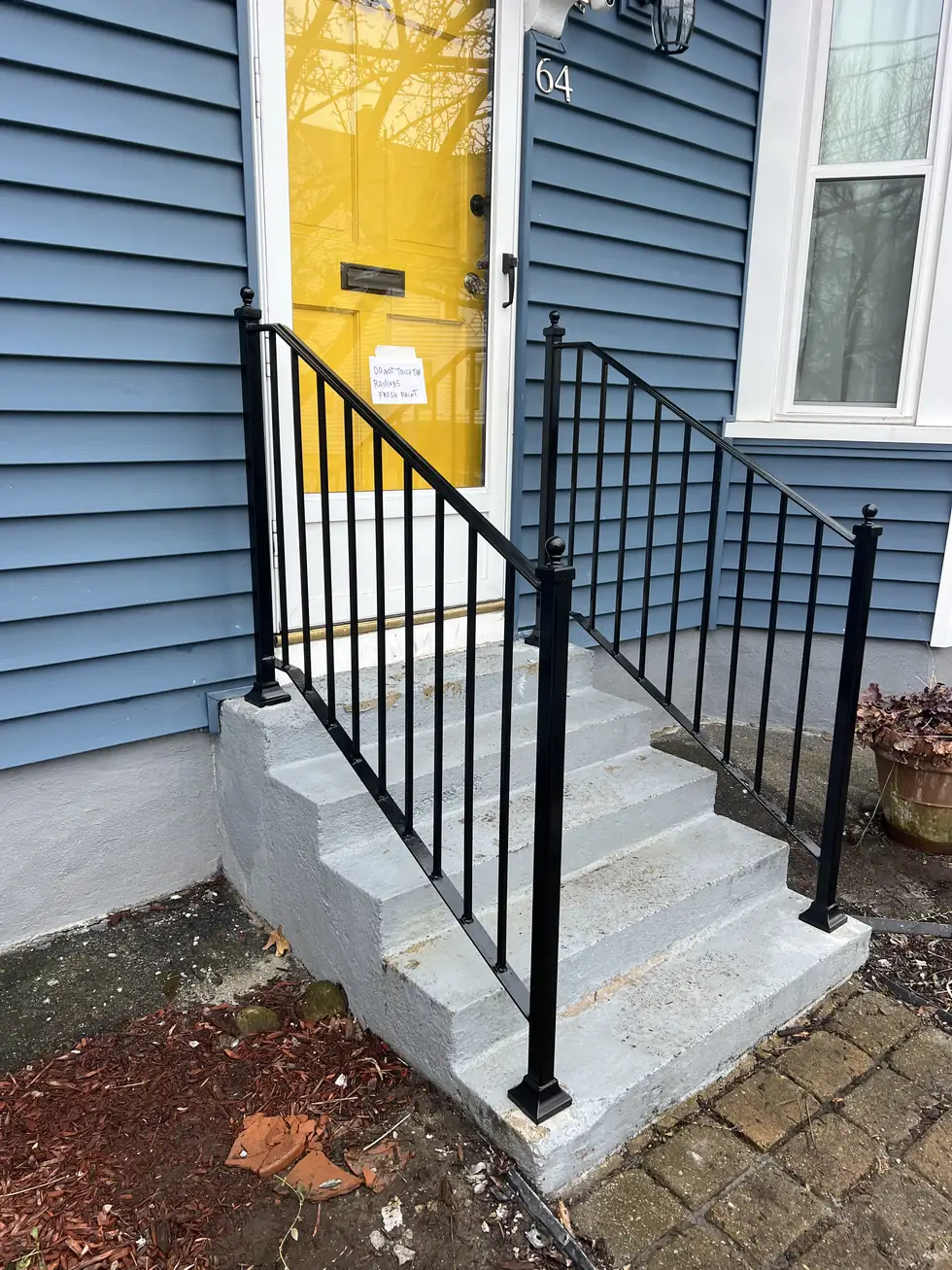 Black iron handrail on entry steps at a yellow door