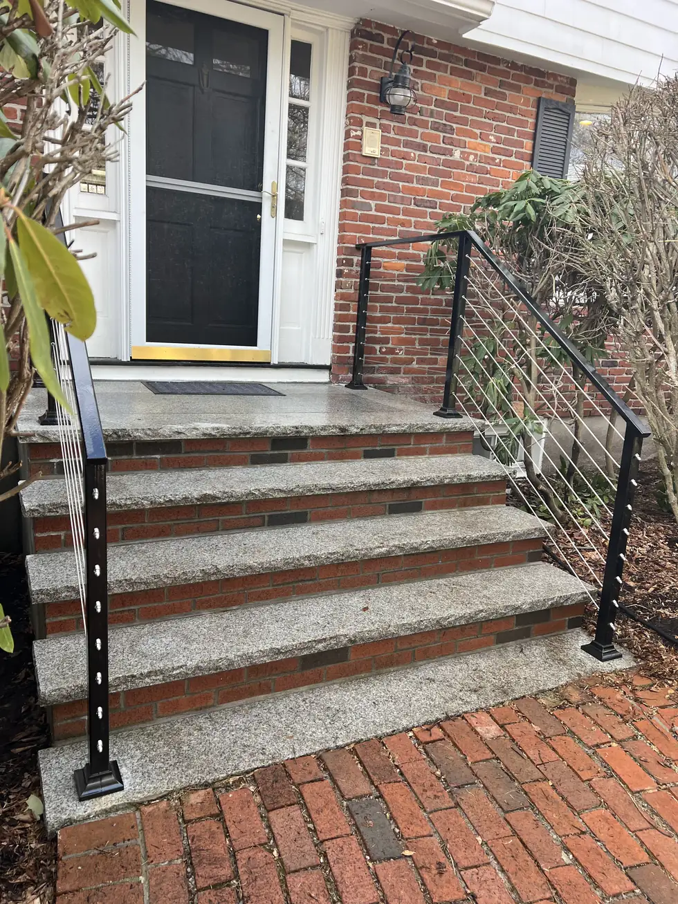 Black steel handrail on brick entry steps at a white door