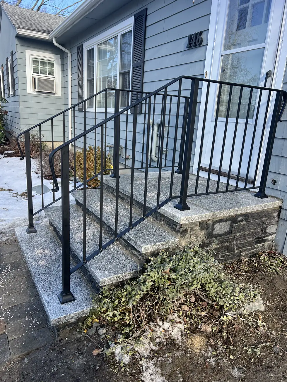 Black steel handrail on granite entry steps at a blue house