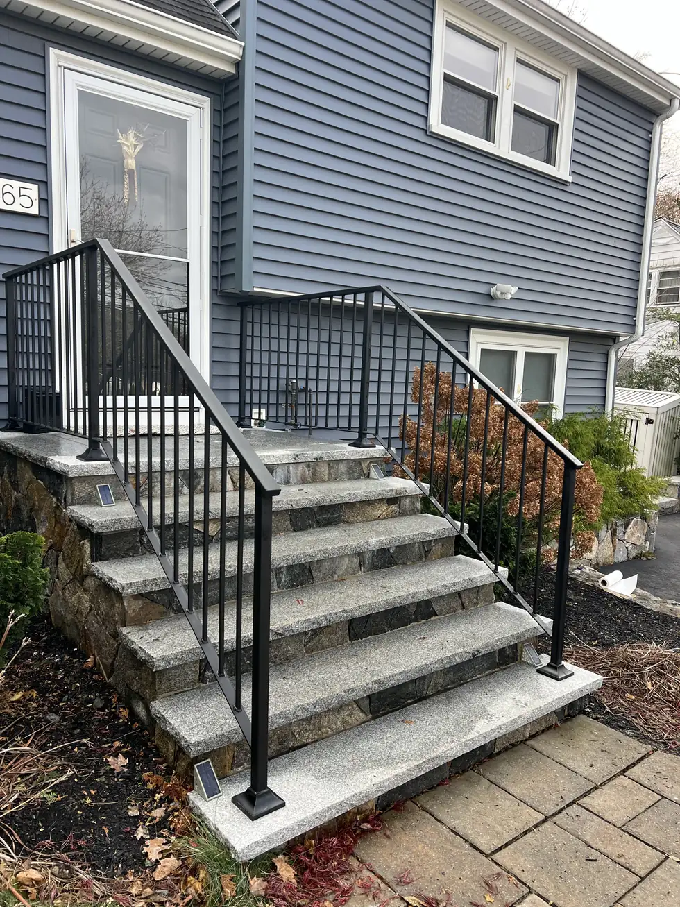 Black steel handrail on granite steps beside a stone wall