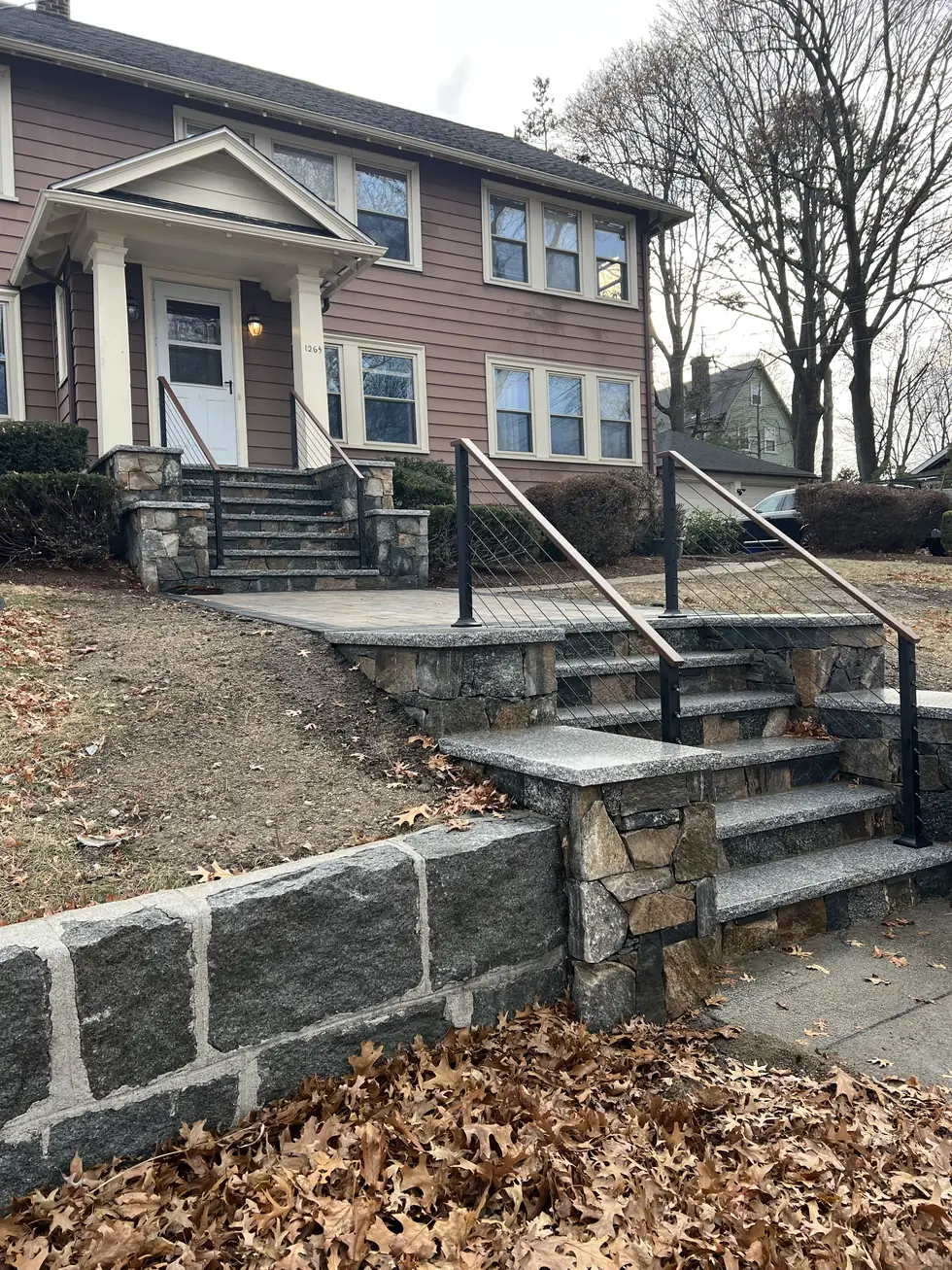 Granite entry steps with a handrail beside a stone retaining wall