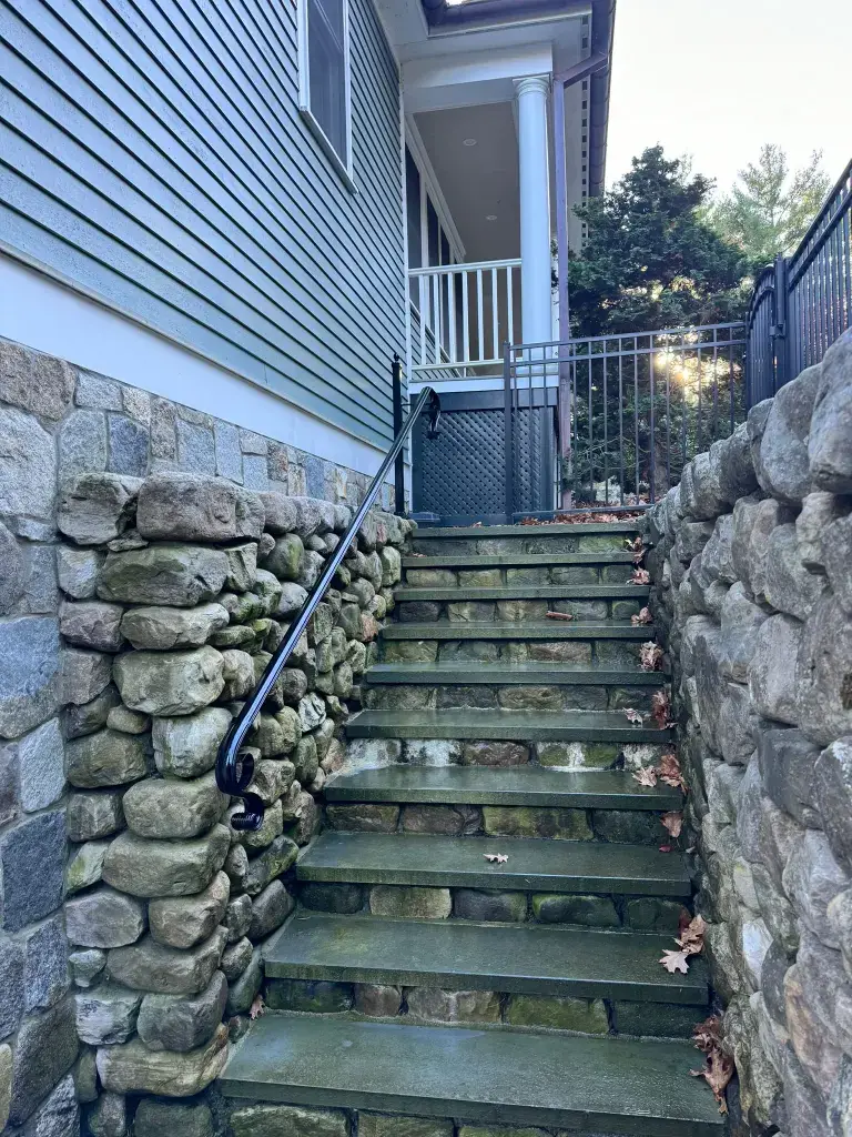 Granite step staircase with iron handrail and stone wall