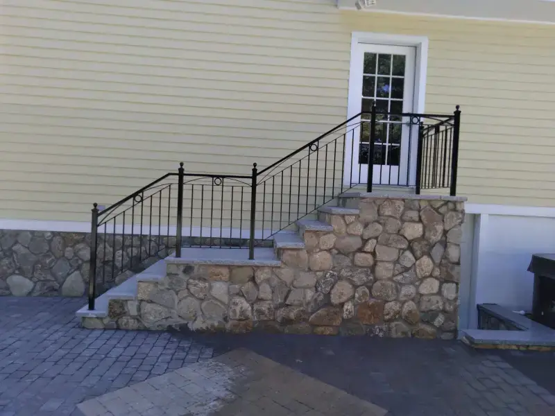 Iron handrail on stone front steps beside a paver walkway