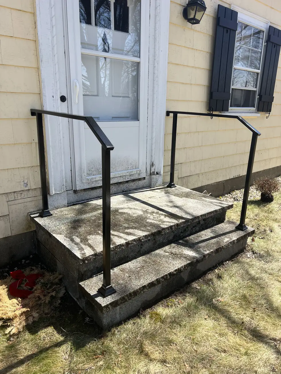 Steel handrail on concrete entry steps at a yellow house