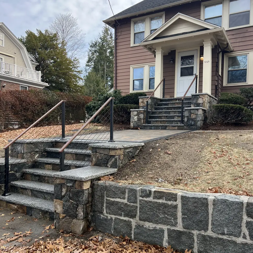 Round tube steel handrail running along granite steps and a stone retaining wall
