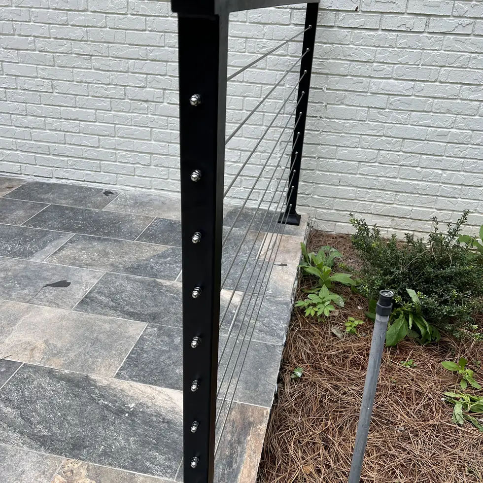 Close-up of a stainless steel cable railing post and swage fittings on a stone patio